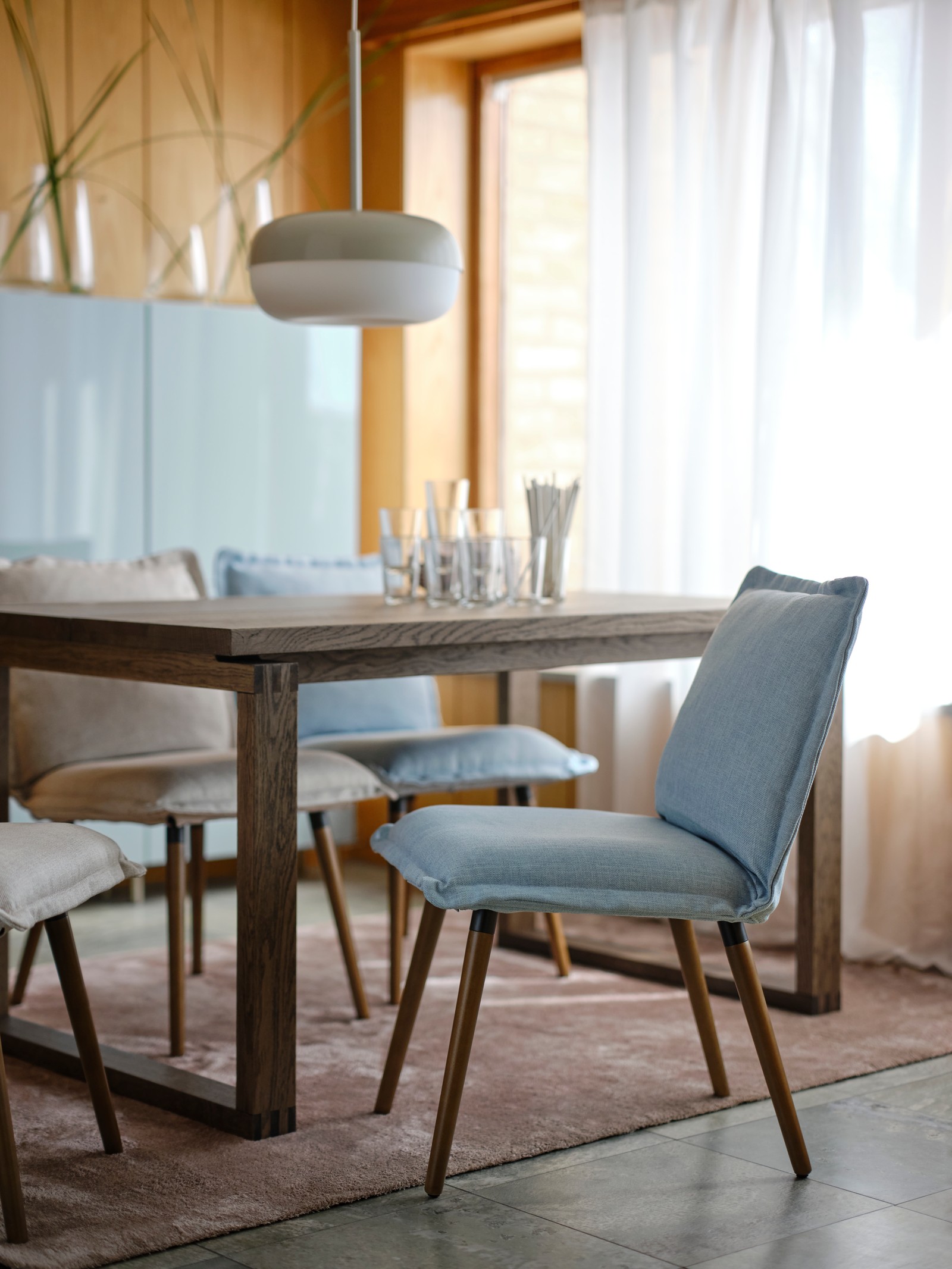 A KLINTEN chair in brown/Kilanda pale blue is pulled out from a wooden dining table in a stylish, sunlit dining room.