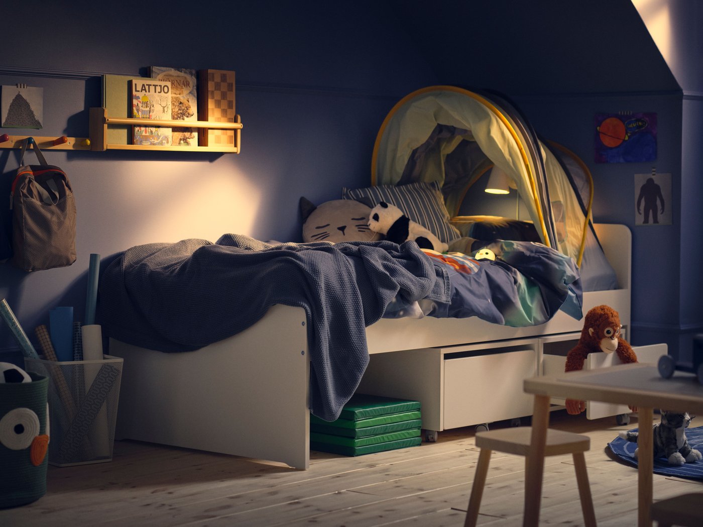 Hoek van een kinderkamer met blauwe wand en gedimd licht, SLÄKT bed met blauw dekbedovertrek en bedtent.