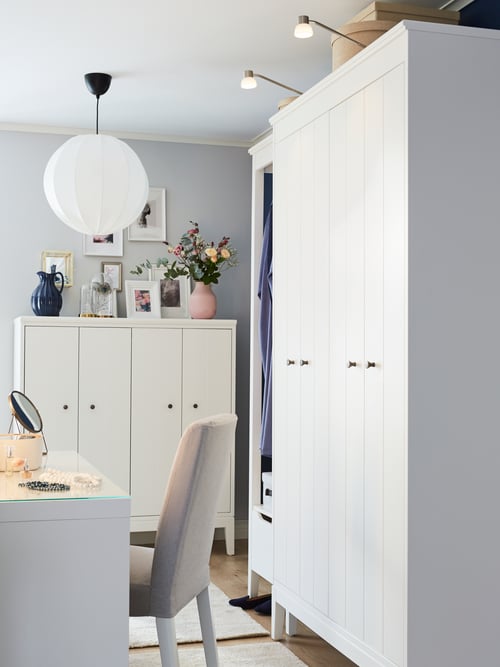 Une coiffeuse blanche, une chaise rembourrée grise, une armoire-penderie blanche avec éclairage intégré sur le dessus, et une suspension blanche.