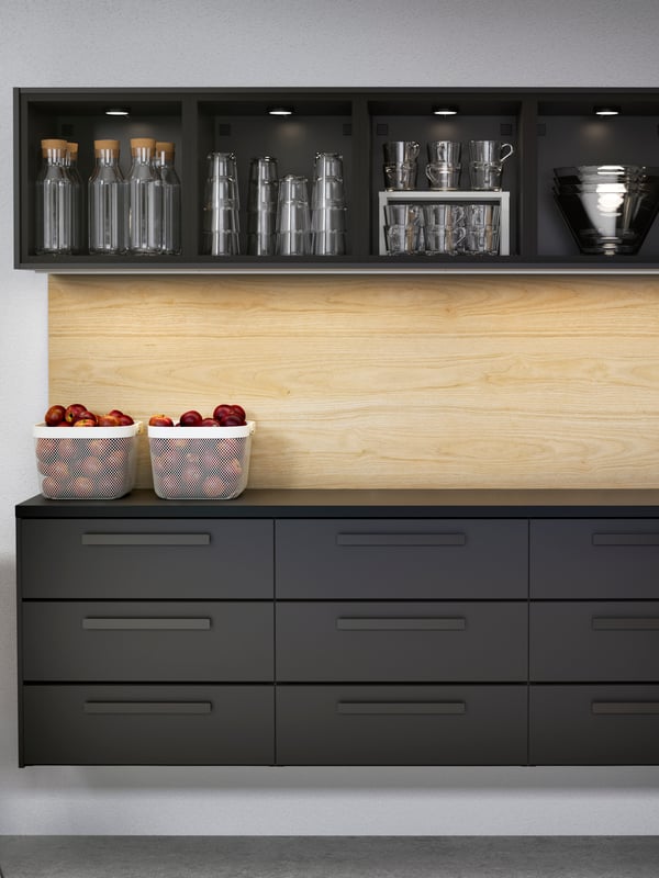 KUNGSBACKA kitchen in dark wood with nine drawers and open upper cabinets with water carafes and glasses.