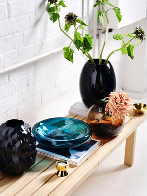 A dark blue-turquoise STOCKHOLM 2025 bowl sitting on a coffee table next to three vases, two of them with flowers.