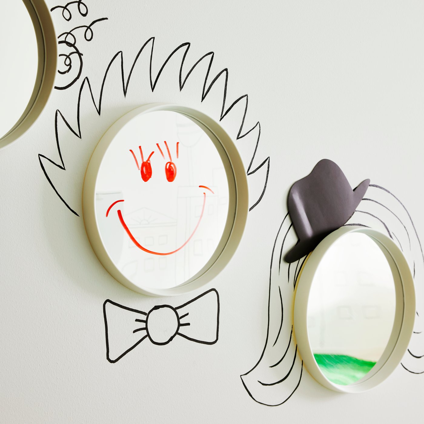 Auf die Spiegelfläche von HÄNGIG Spiegeln sind Frisuren, Hüte und lächelnde Gesichter aufgemalt.