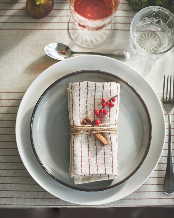 A plate setting with stripe pattern red/natural VIPPSTARR napkin folded on top.