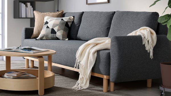 Mörkgrå GRUNNARP bäddsoffa med träben och pläd placerad i en modern vardagsrumsmiljö.
