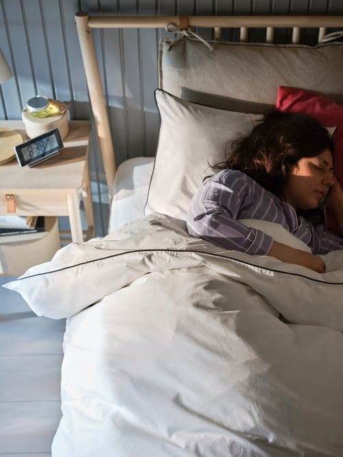 A young girl sleeping in a bedroom that features a bed frame, a bedside table, and a duvet cover with two pillowcases.