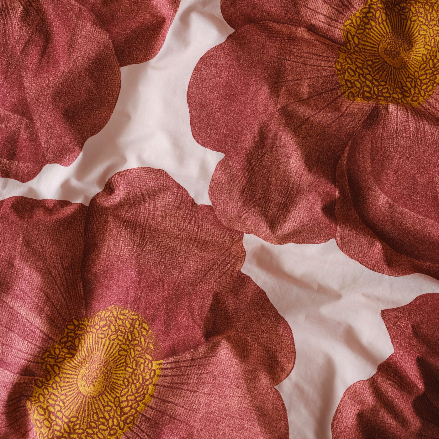The bold floral print of a SVARTKLINT duvet cover in light pink/dark pink covering a duvet that’s a bit rumpled.