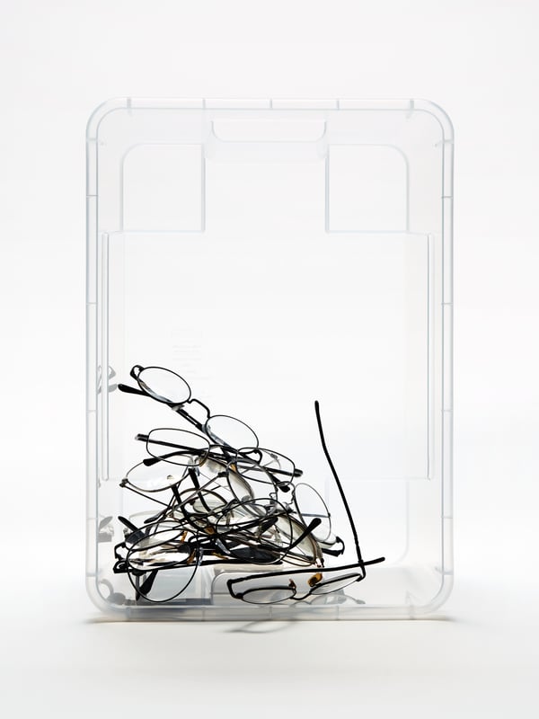 A transparent SAMLA storage box standing vertically with a pile of reading glasses in the left-hand corner.