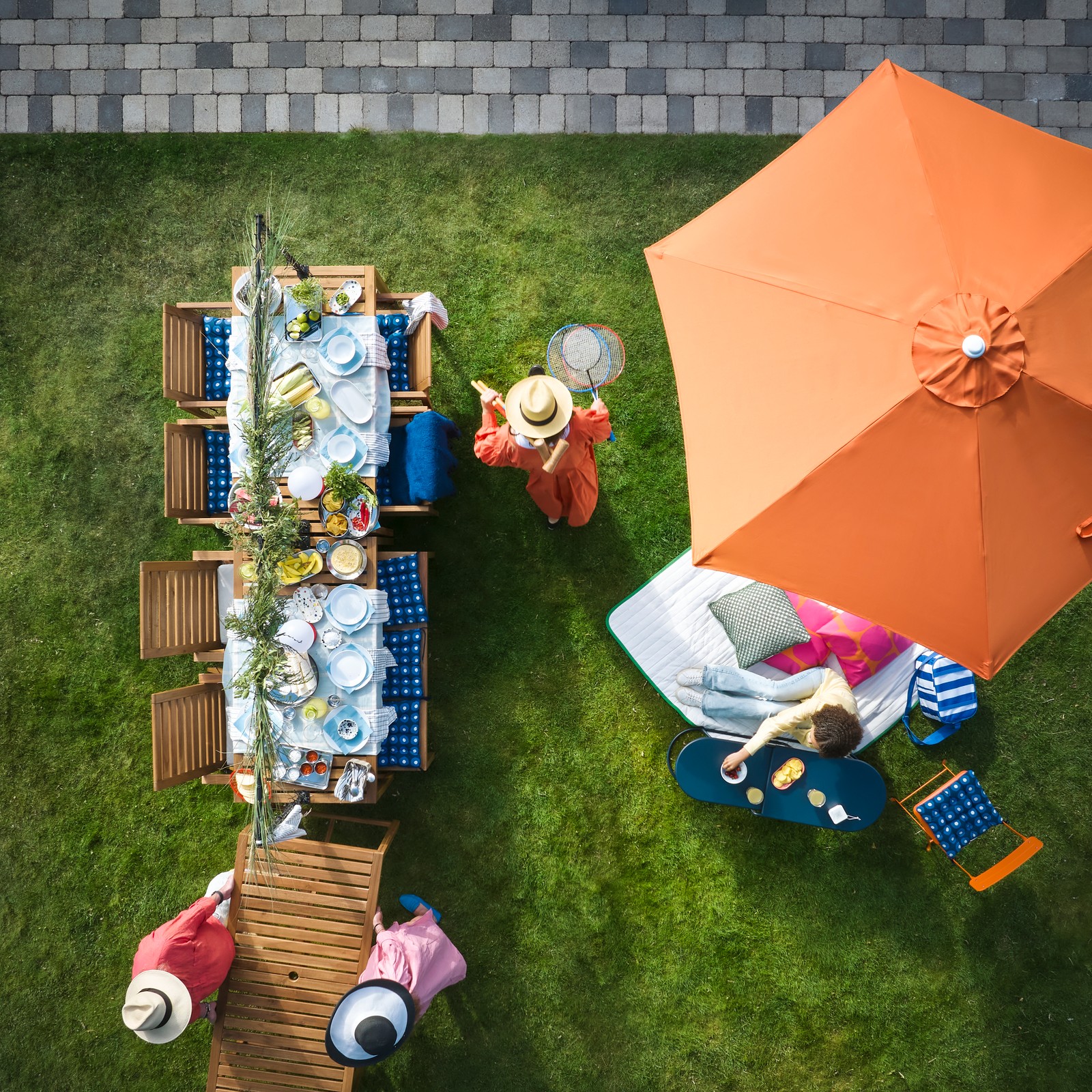 A garden with outdoor seating features a light brown stained NÄMMARÖ table surrounded by people enjoying refreshments.