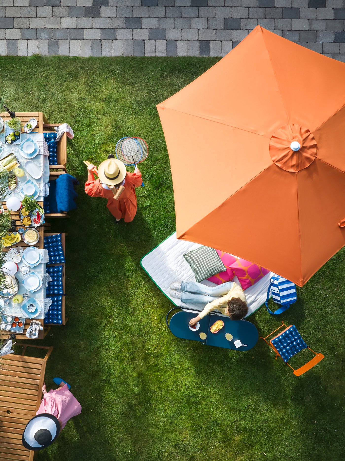 A garden with outdoor seating features a light brown stained NÄMMARÖ table surrounded by people enjoying refreshments.