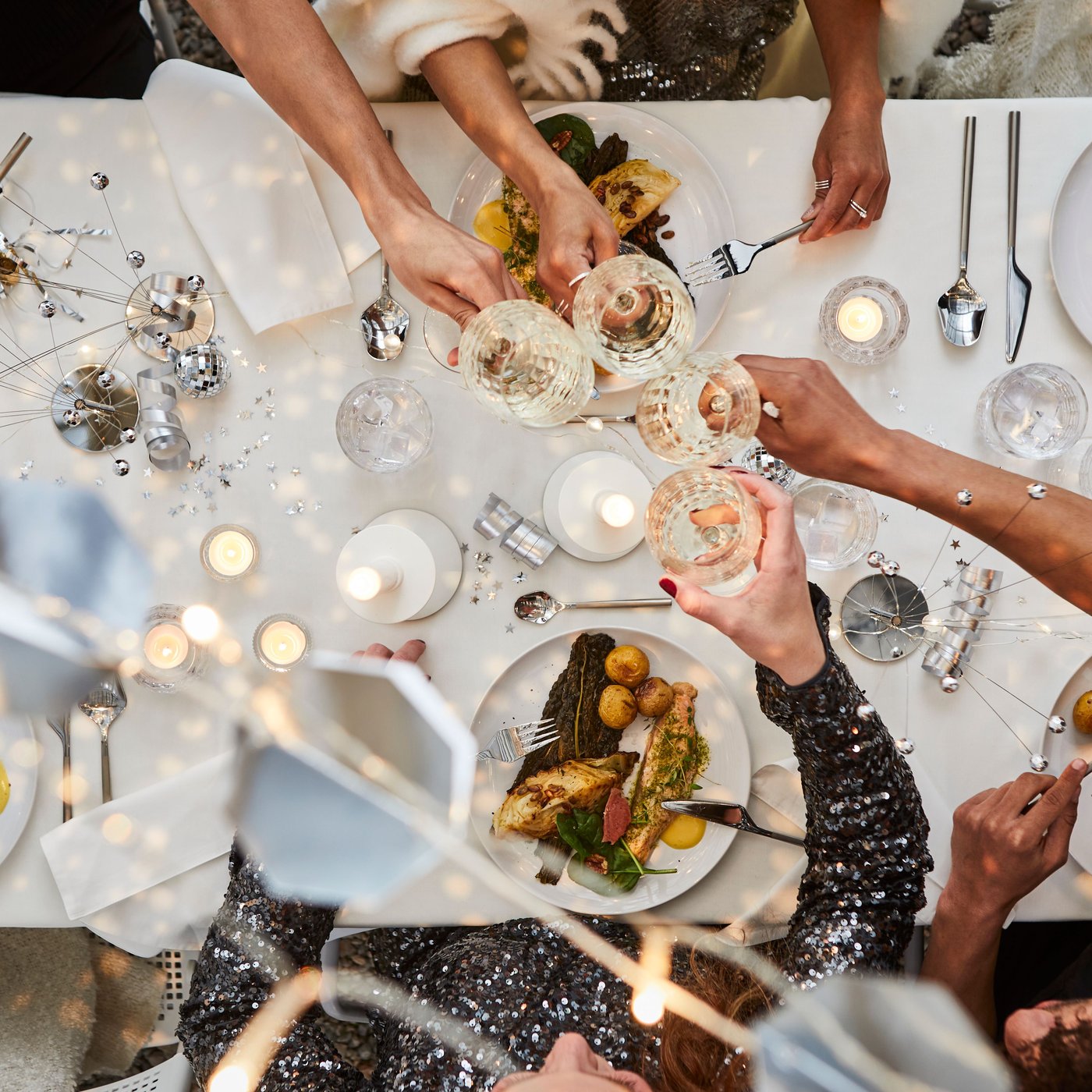Vogelperspektive auf die silber-weiße Silvestertischdekoration, Anstoßen mit FRÖJDA Champagner-Coupés.