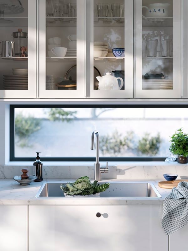 Cabinets with HEJSTA glass door are mounted above a VRESJÖN inset sink and an ÄLMAREN kitchen mixer tap in stainless steel.