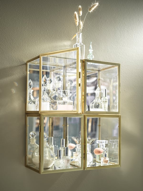 Four wall-mounted, gold-colour BOMARKEN display boxes grouped together and filled with decorative glassware.