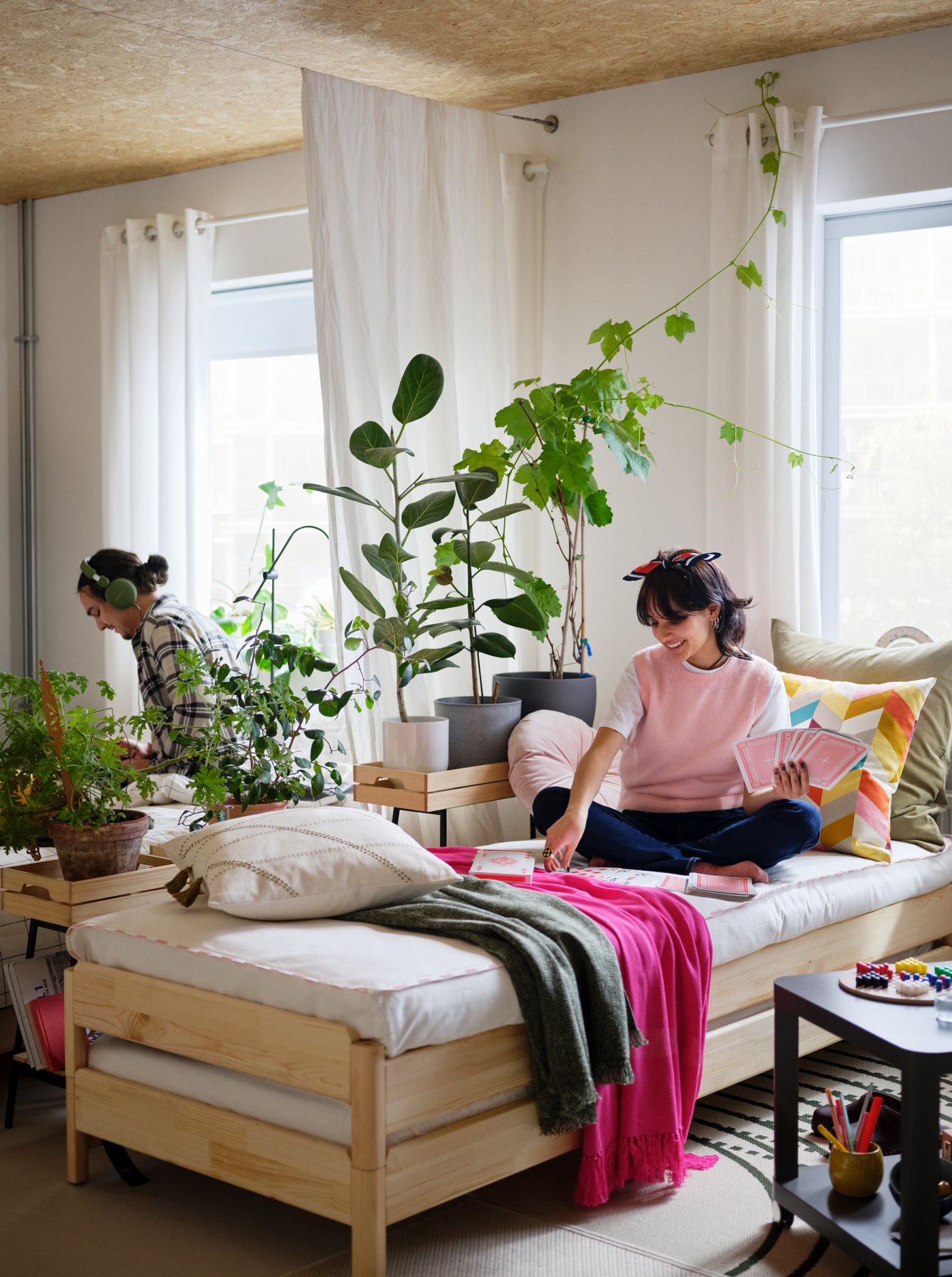 Une fille est assise sur un lit superposable UTÅKER, recouvert de différents plaids et de linge de lit.
