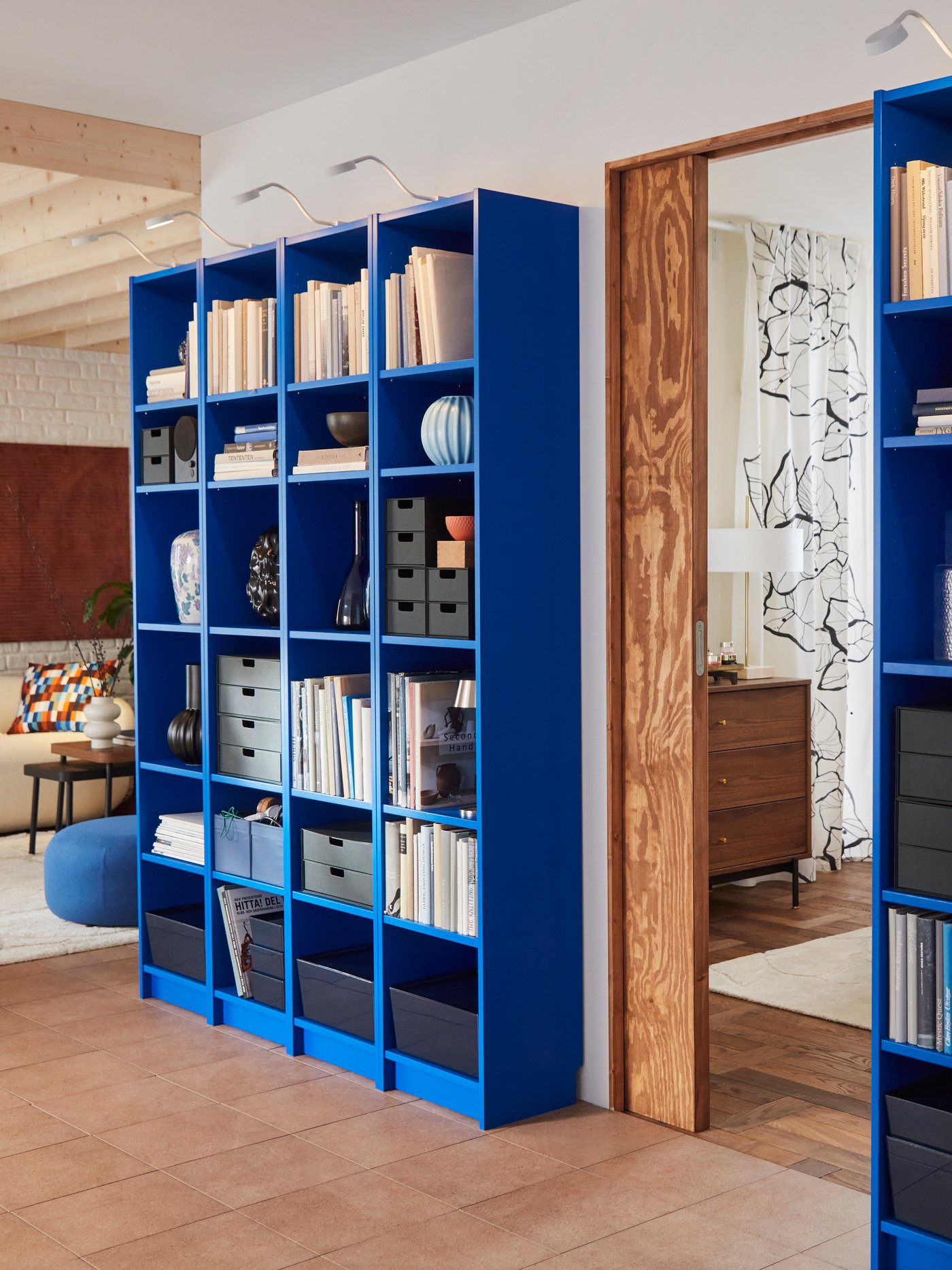A living room features two blue BILLY bookcases filled with books and decorative items, beside a doorway.