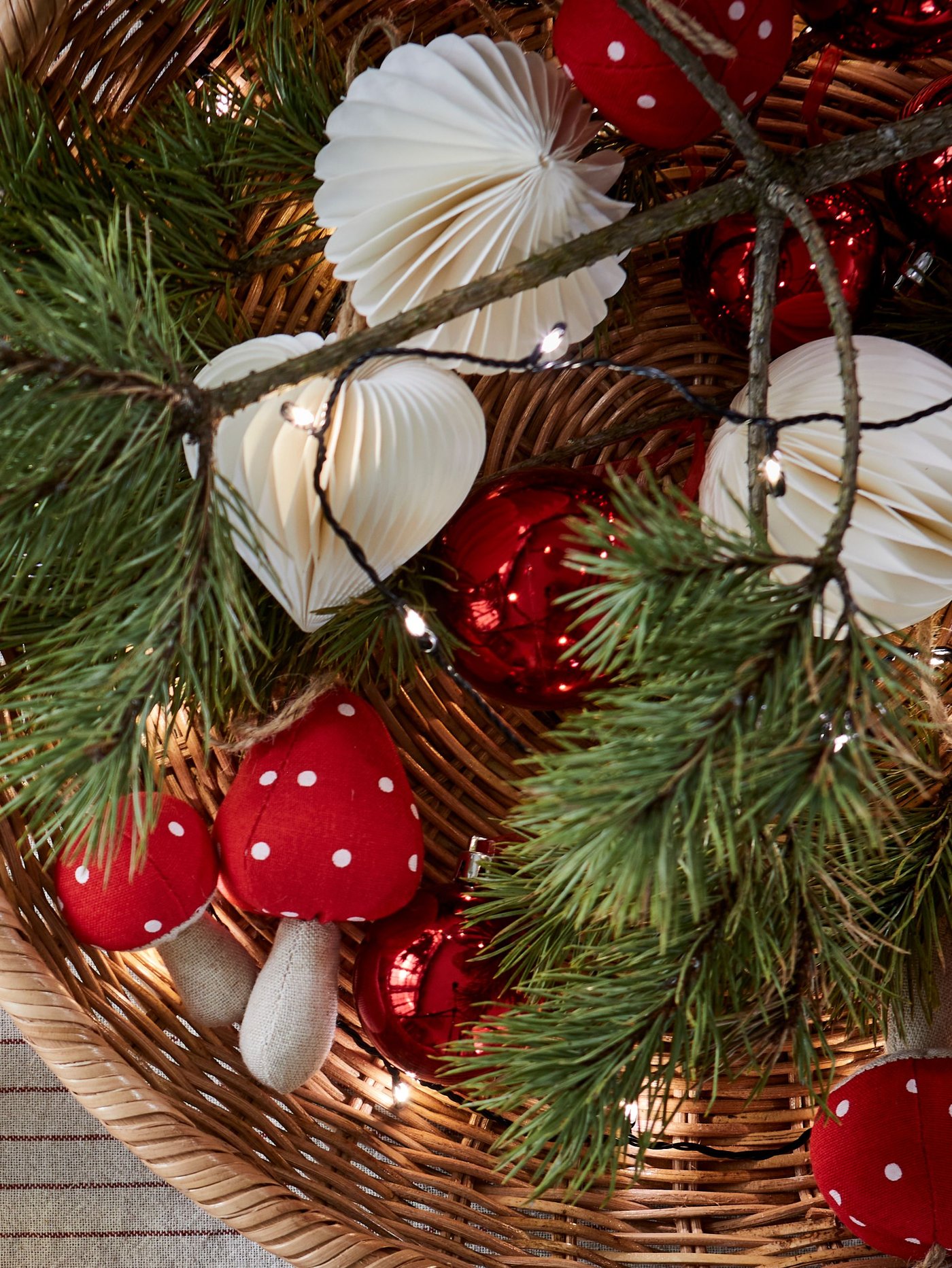 Close-up of VINTERFINT tree ornaments including white paper bell and toadstool in a basket with pine.