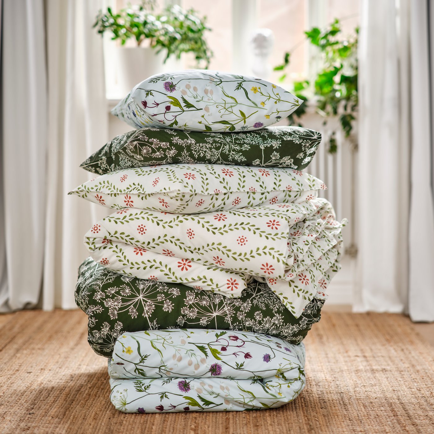 A bedroom showcasing a stack of FYRISVIDE, MATTOXBÄR and DAGGBJÖRNBÄR duvet covers and pillowcases on a jute rug.