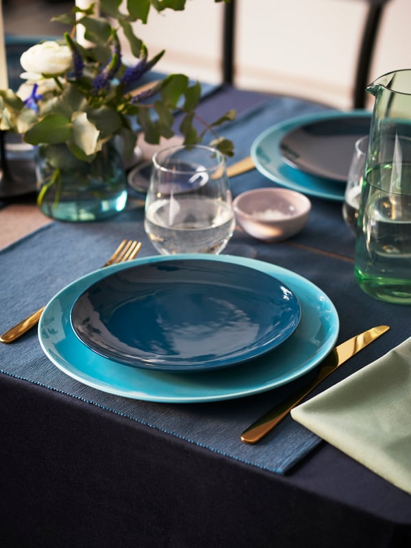 A small wedding table is set with dark and like blue dinnerware with flowers placed as a centre piece.  