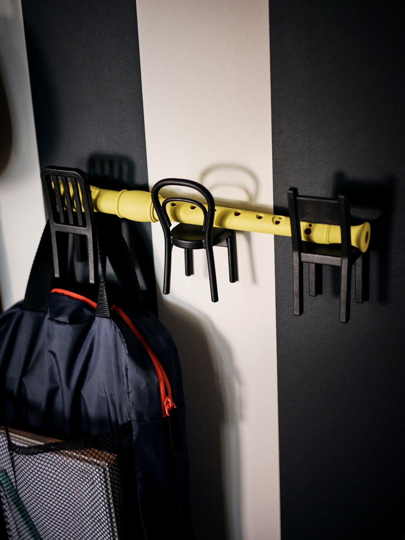 Tres ganchos FJANTIG con forma de sillas instalados uno al lado del otro. Sostienen una flauta de forma horizontal y en uno cuelga un bolso.