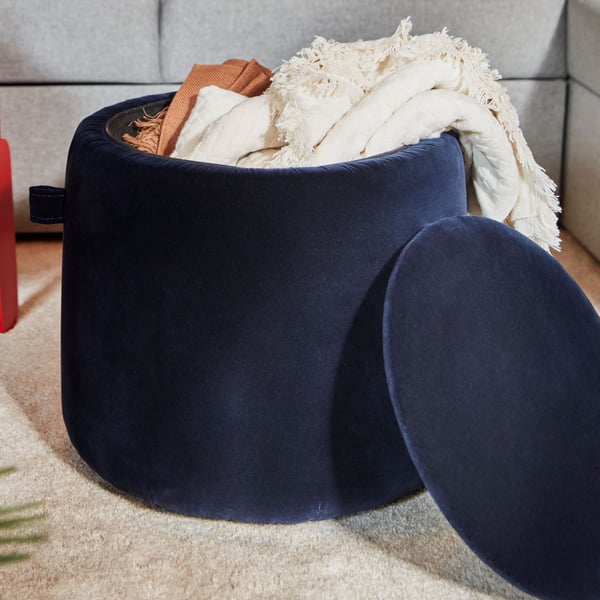 A red FÖRLUNDA pouffe with storage and a dark blue JÄRRESTAD pouffe with storage containing throws stand near a sofa.
