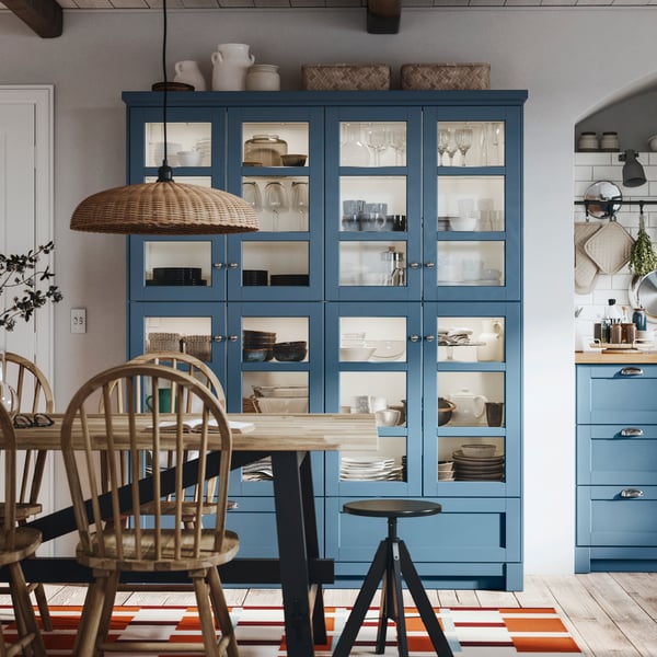 A dining table is standing in front of a piece of furniture made of SEKTION cabinets with glass doors in LERHYTTAN blue.