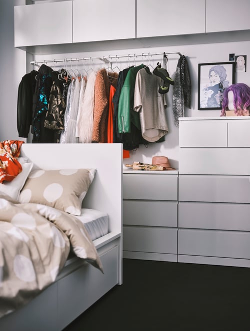 Bedroom with a white, high bed frame with storage boxes, a duvet set, white chests with drawers, and a clothes bar.
