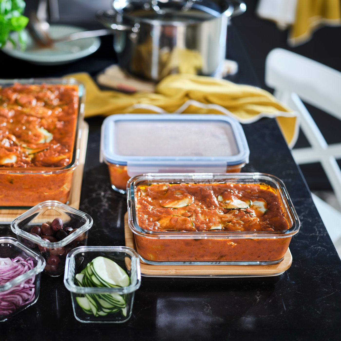 Sur un comptoir noir, contenant alimentaire IKEA 365+ contenant des lasagnes, parmi des légumes et d’autres plats.