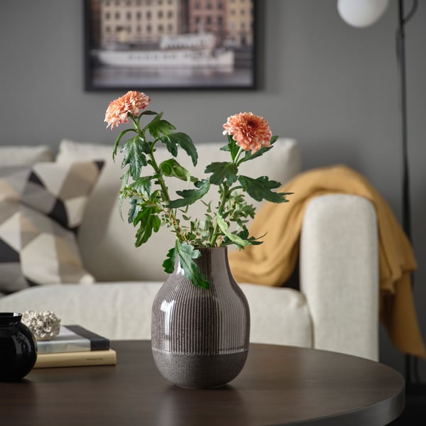 A dark grey GRADVIS vase with two flowers in of the coffee table in the living room.