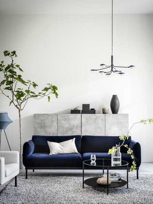 Salon avec un canapé trois places avec un coussin, un lustre à DEL, un lampadaire turquoise et une table basse ronde.