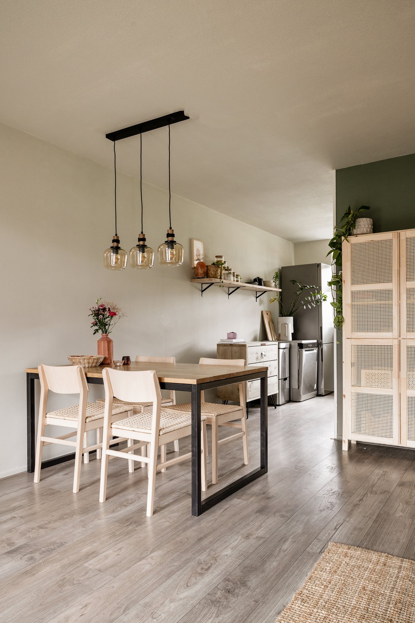 Een woonkamer met daarin een tafel, vier stoelen en de keuken op de achtergrond.
