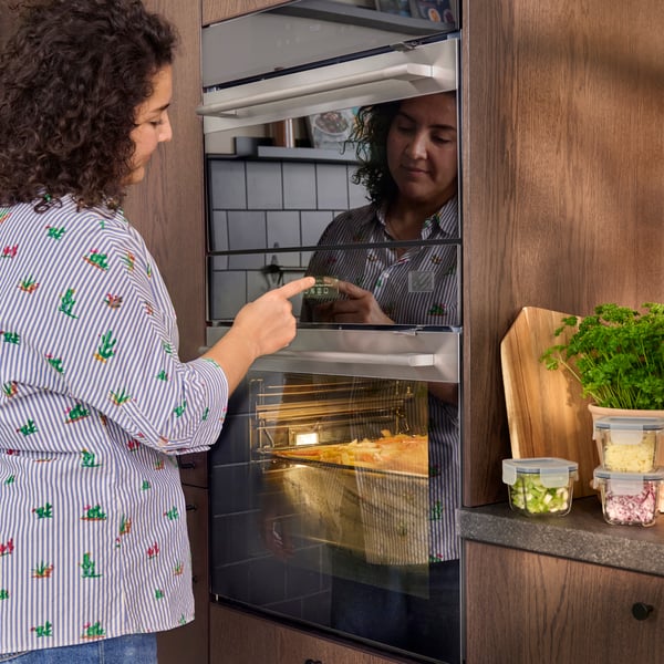 Een persoon staat bij een FRILLESBO oven met magnetronfuctie en raakt het scherm aan.
