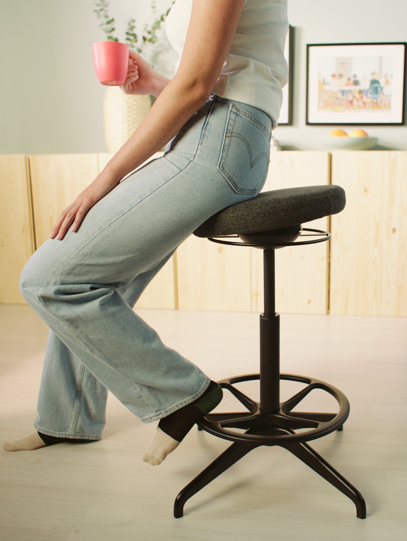 Woman holding a pink mug leaning on LIDKULLEN ergonomic stool.