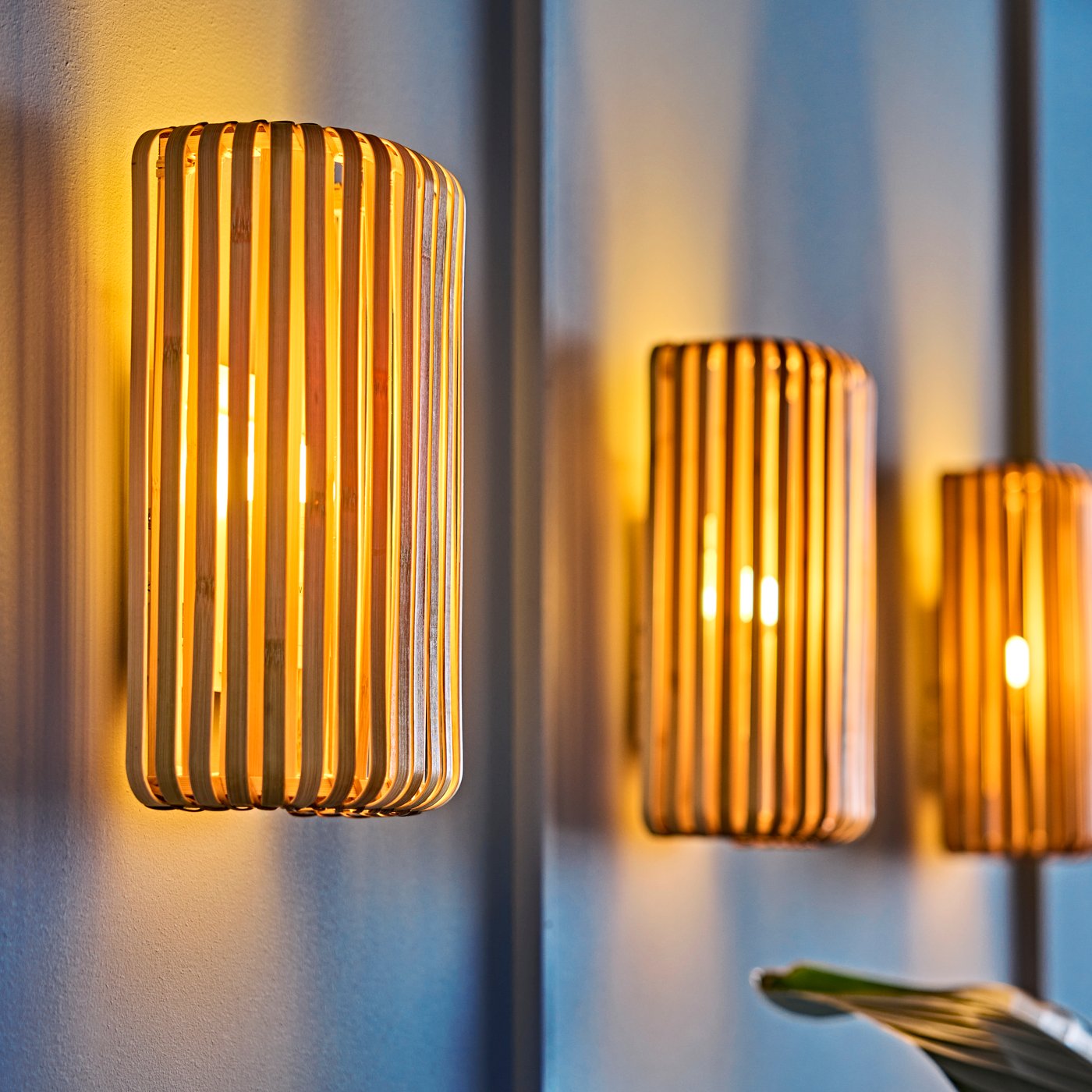 A blue living room wall with warm glow from three natural colour VARPTROSS wall lamps made from bamboo.
