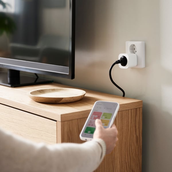 A white power outlet in a wall, a man holding an IKEA Home smart remote control in front of the outlet.