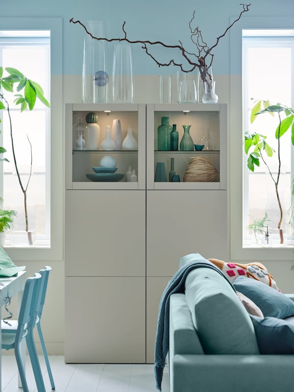 BESTÅ storage combination with glass doors against a wall between a dining area and a sofa.
