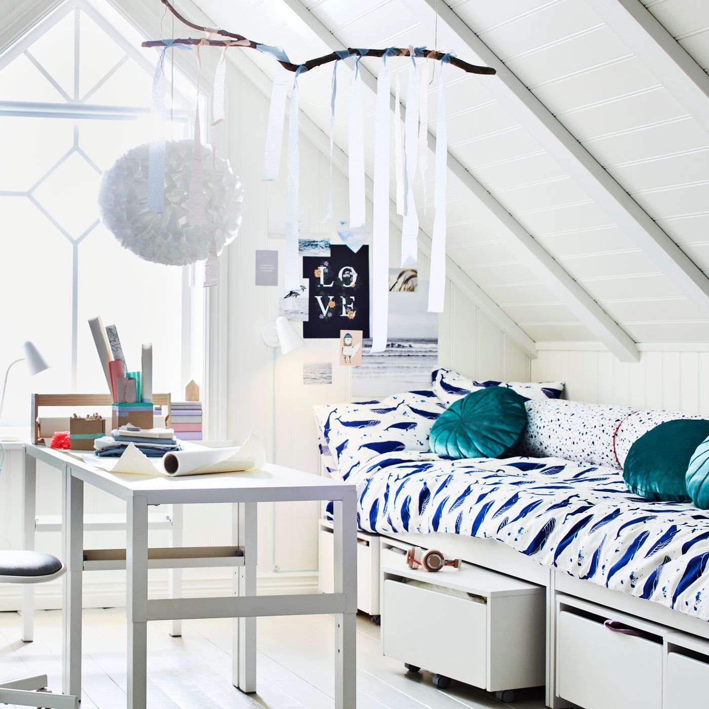 Ett rum med ett sluttande tak och ett stort fönster. Två PÅHL skrivbord står i mitten nära två sängar och lite TROFAST förvaring.