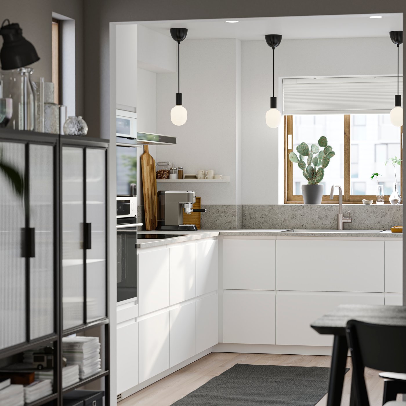 Ett litet kök med släta vita VOXTORP fronter, vita väggar, en grå matta på golvet och tre små svarta pendellampor.