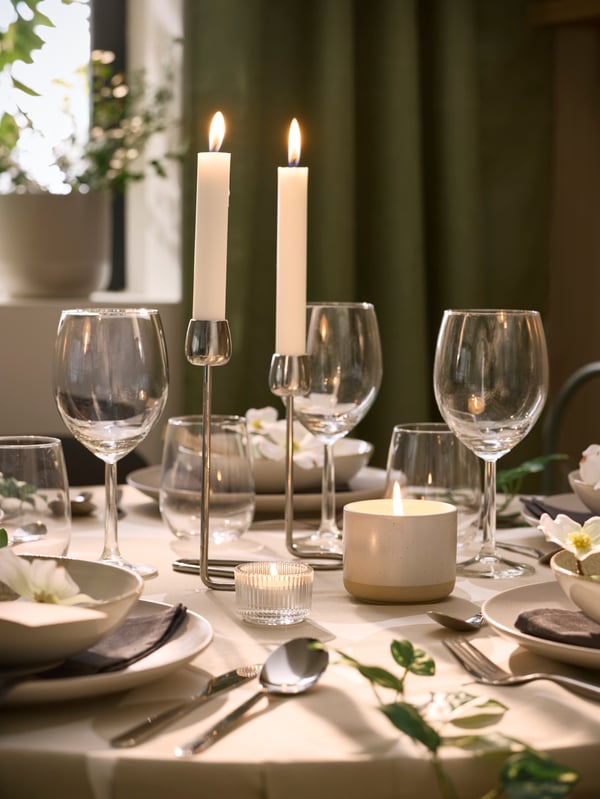 A festively table with a JÄMLIK scented candle and lit candles in a FINSMAK tealight holder and a SILVERPÄRON candlestick.