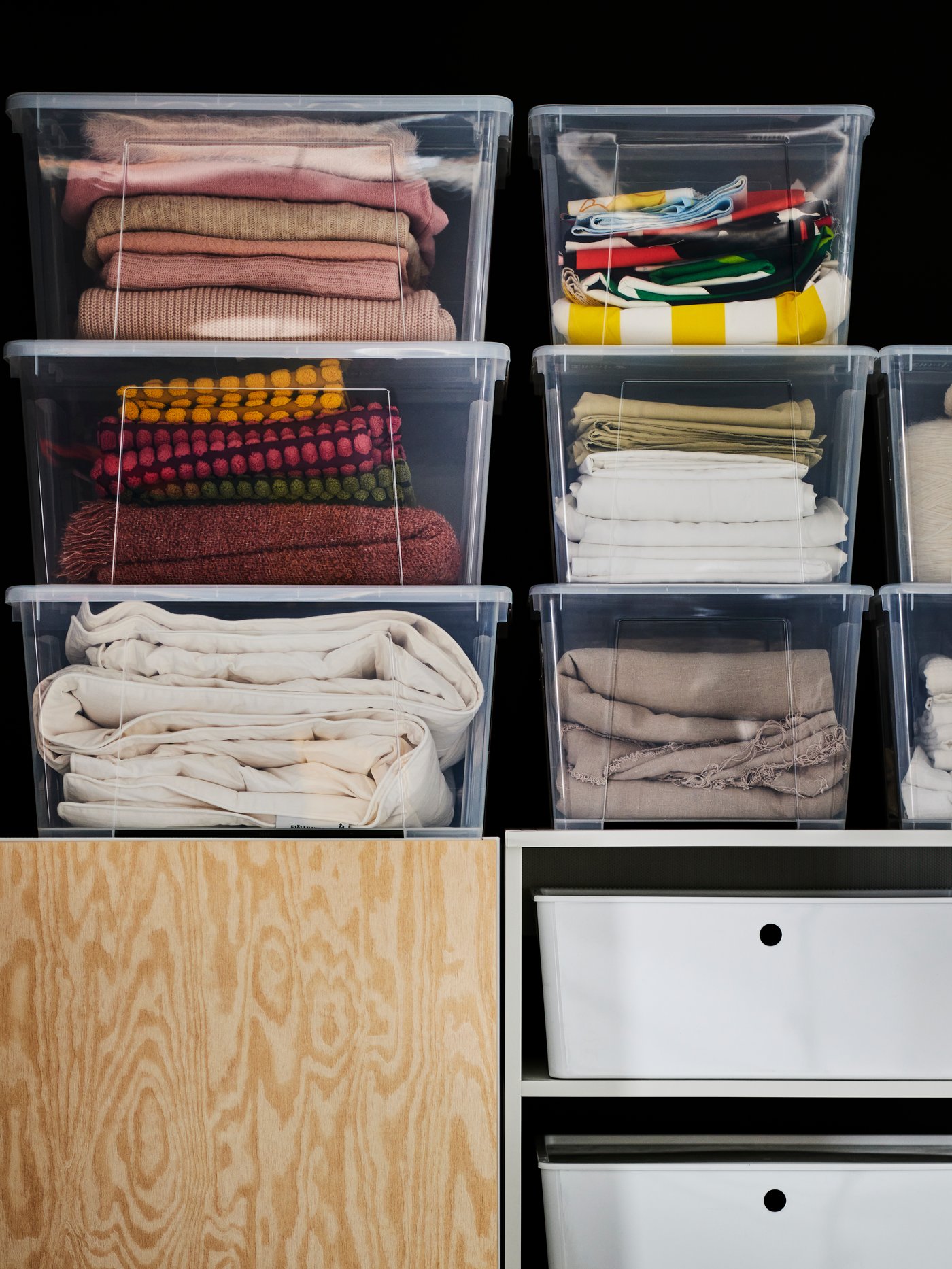 Transparent SAMLA boxes with clothes are neatly stacked on top of one another on a PLATSA open shelving unit. White KUGGIS boxes are placed in the open PLATSA shelves.