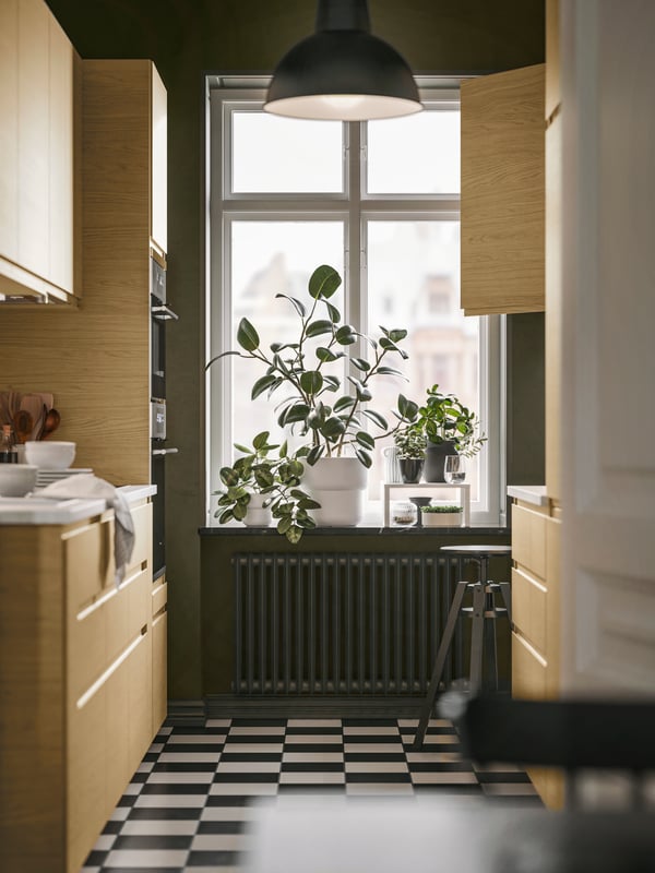 A parallel kitchen with VOXTORP fronts in oak effect and with integrated handles has a window with plants on the windowsill.