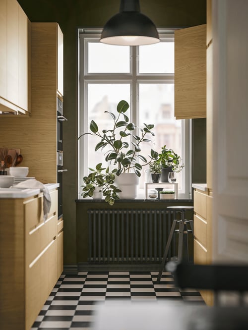 Kitchen with multiple beige VOXTORP doors, a black SKURUP pendant lamp, a FÖRENLIG plant pot and a DALFRED bar stool.
