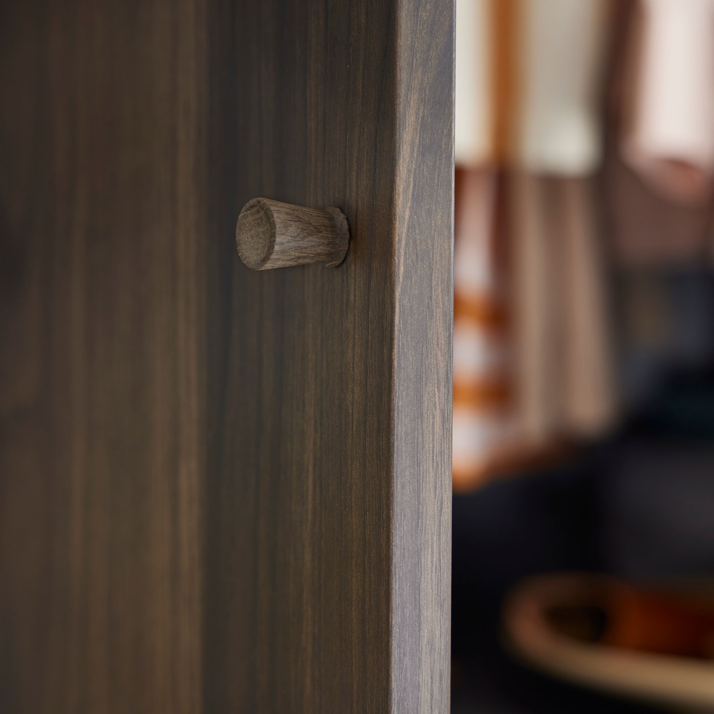 A close-up of a solid oak TÄRNESTAD knob attached to a dark brown oak effect STORKLINTA door.