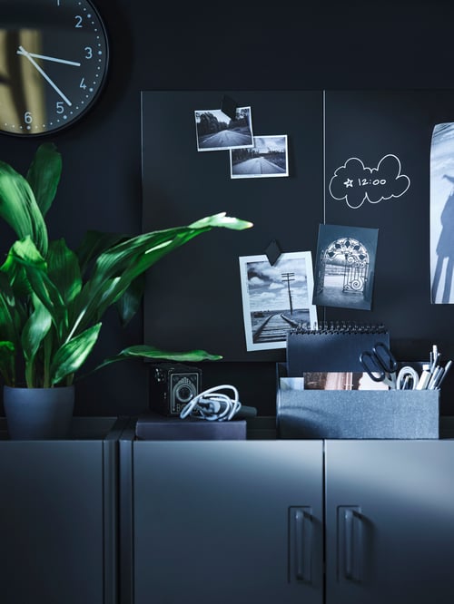The top of two IDÅSEN cabinets with two SVENSÅS memo boards on the wall holding photos and with writing in chalk on it.