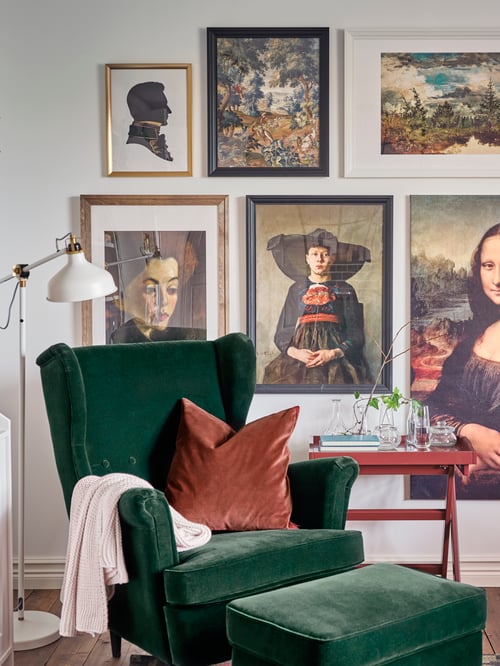 Cameră de zi artistică amenajată cu un scaun elegant cu aripă verde închis și o pernă pătrată moale, în fața afișelor de artă înrămate.