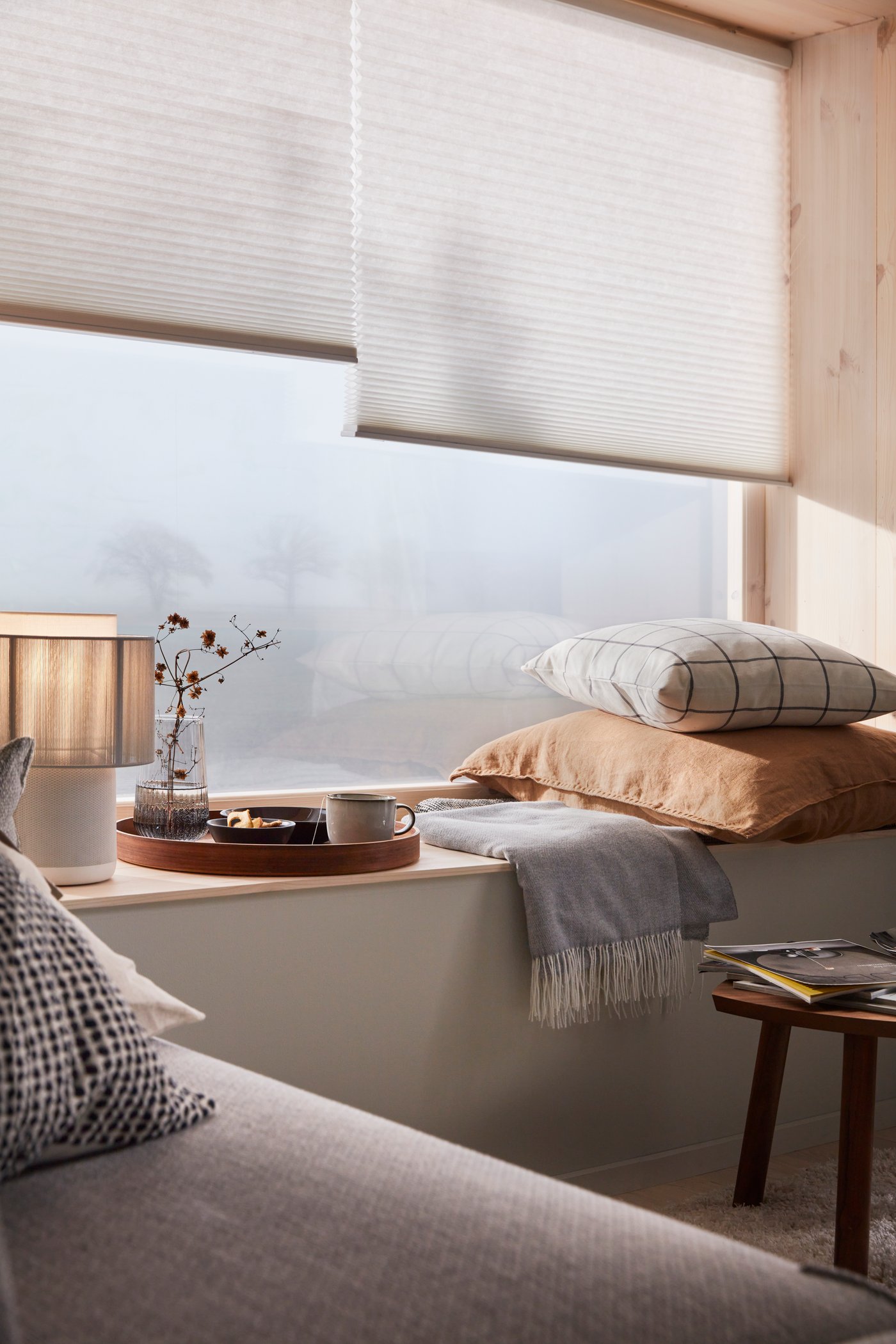Een vensterbank in een Japandi woonkamer met twee witte rolgordijnen voor het raam.