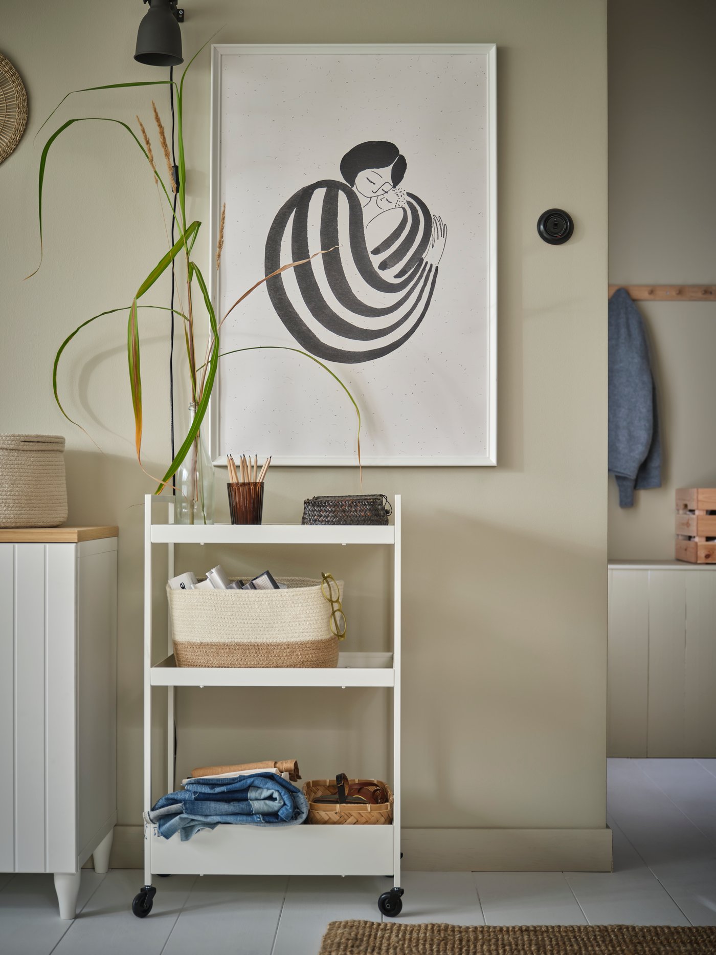 Une grande affiche d’une femme sur un mur beige. Une desserte blanche remplie d’accessoires se trouve dessous.