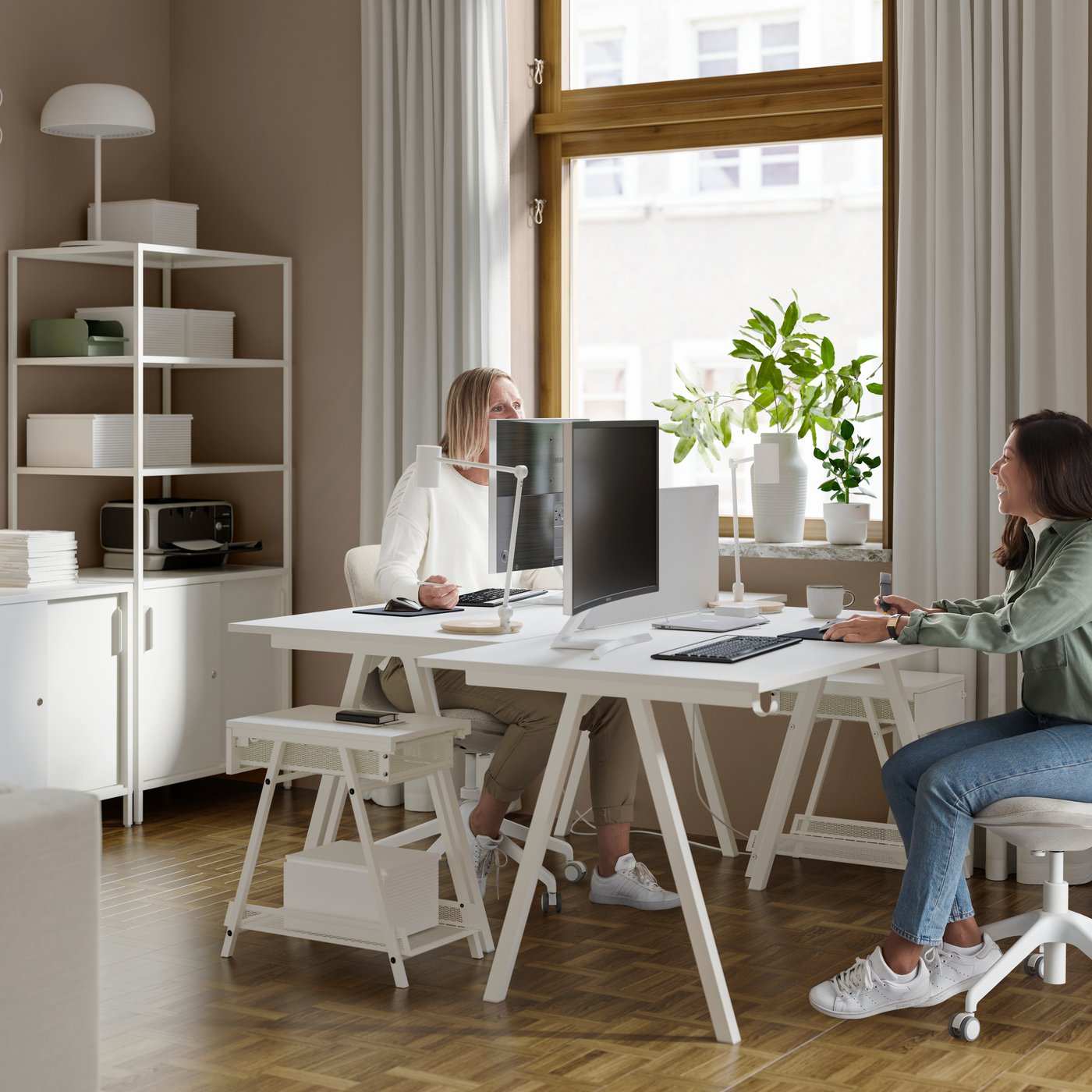 Två personer i ett kontor med öppen och stängd förvaring, hyllor som rumsavdelare, skrivbord och kontorsstolar.