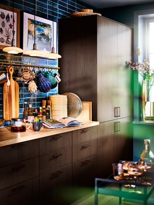 A SINARP kitchen with a blue-green tiled wall, with pendant lamps above a worktop with kitchen accessories.