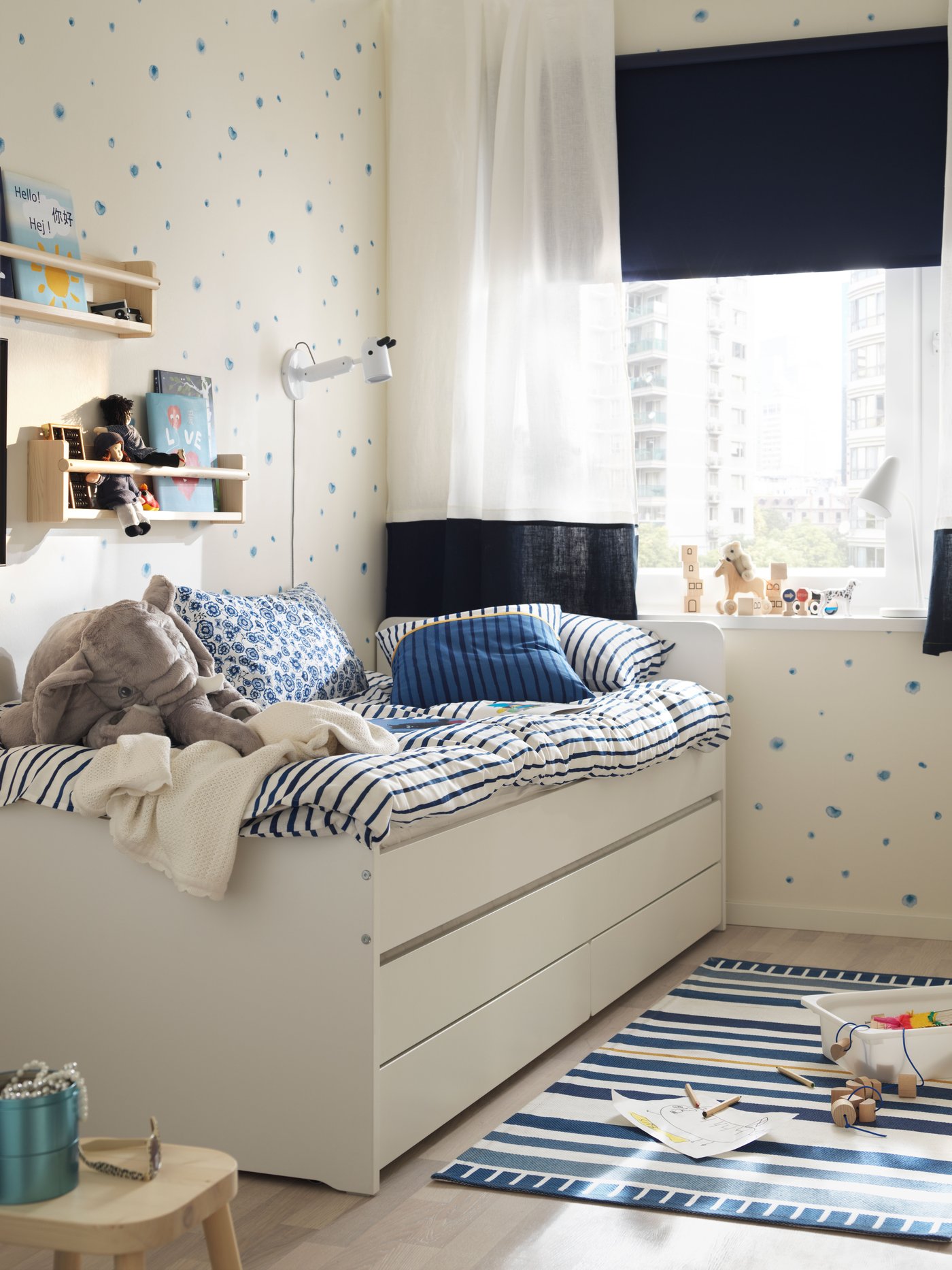 Dormitorio con estructura de cama con cama inferior y almacenaje, cojines, una lámpara de pared LED, un almacenaje de pared y un estor opaco.