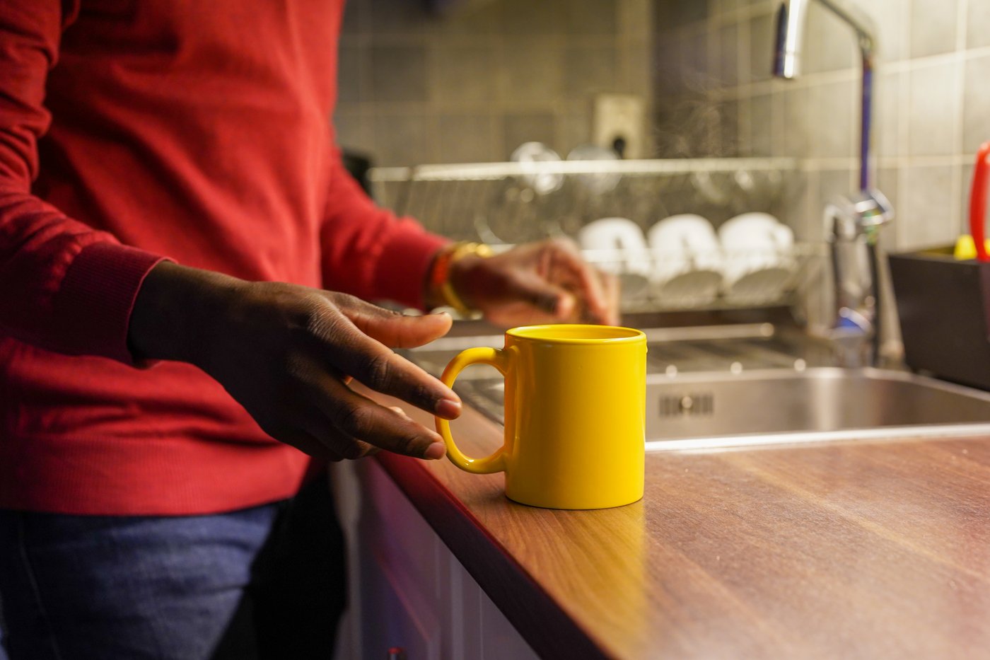 A photo of a yellow cup and a person reaching for the cup.
