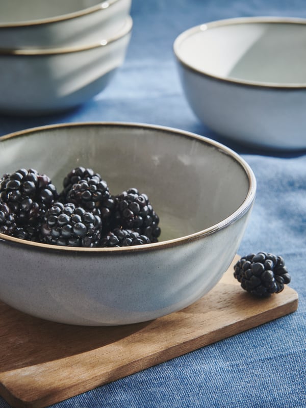 Gray GLADELIG bowls scattered across a blue tablecloth. One stands on a small chopping board and is filled with blackberries.